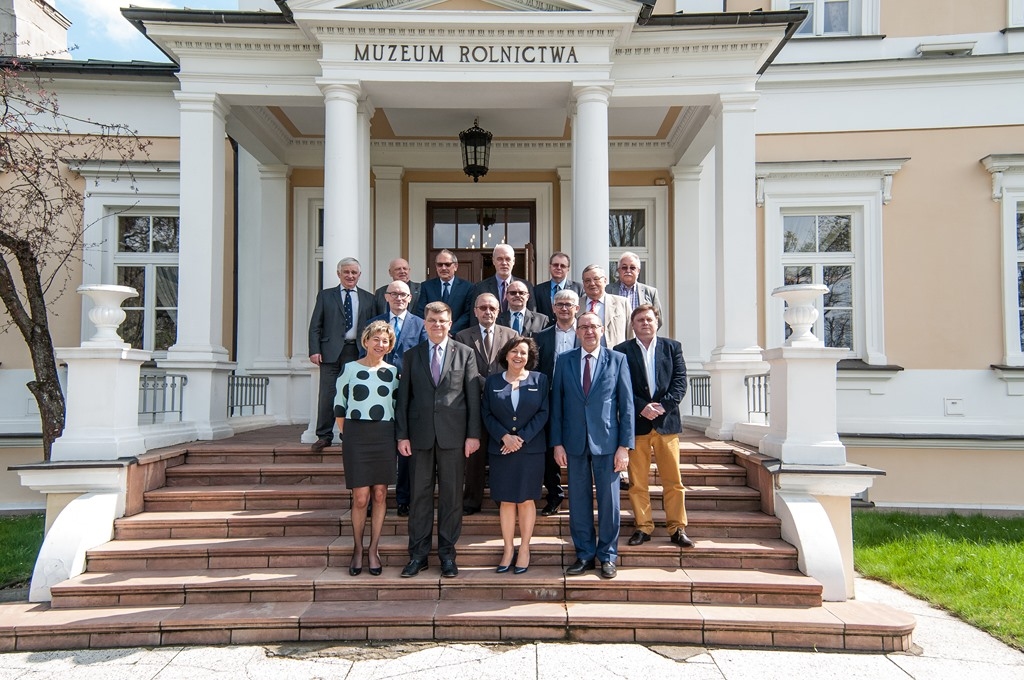 Grupa formalnie ubranych osób stoi na schodach przed neoklasycystycznym budynkiem z napisem „Muzeum Rolnictwa”.