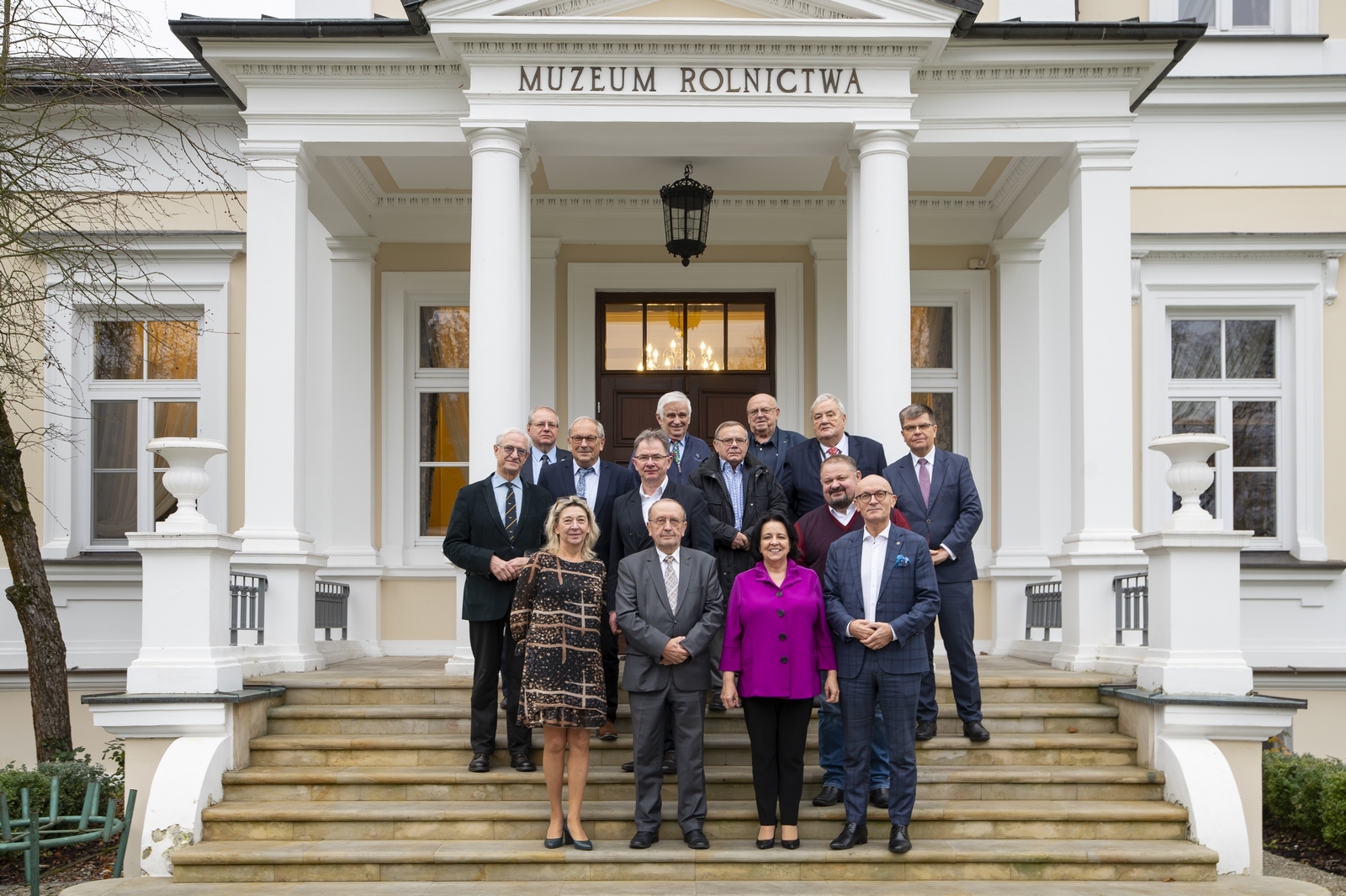Grupa ludzi stoi na schodach białego budynku z napisem „Muzeum Rolnictwa”.