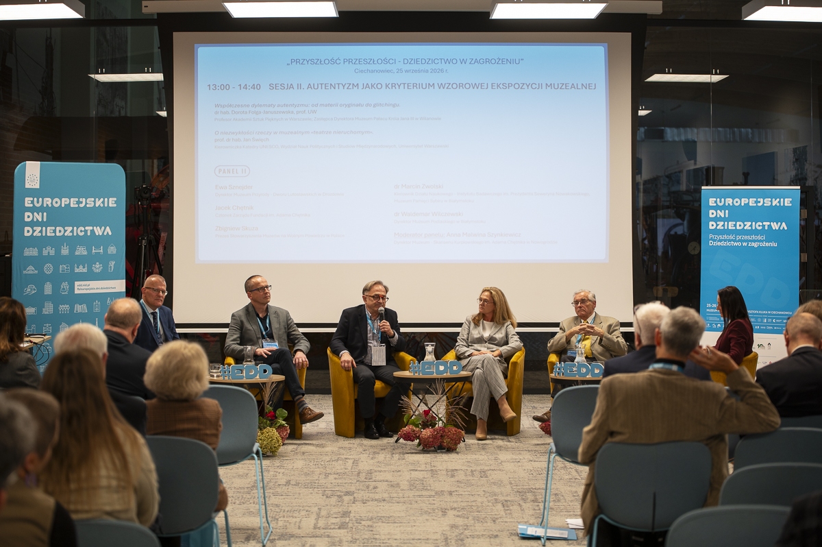 Szeroki kadr przedstawiający salę konferencyjną w trakcie trwania sesji panelowej, z widoczną publicznością oraz prelegentami na scenie.