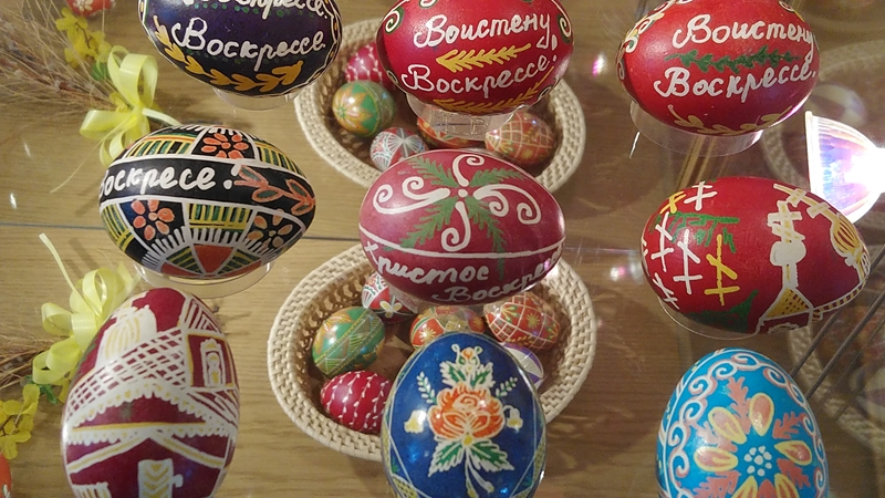 Jaskrawo zdobione pisanki o misternych wzorach i motywach kwiatowych w różnych kolorach są ułożone na drewnianym stole, przekazując świąteczną atmosferę.