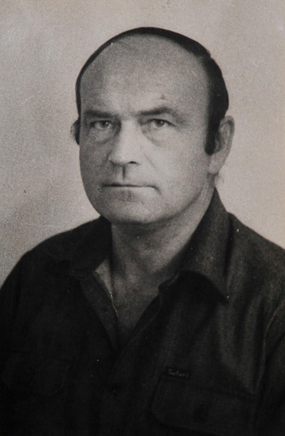 Czarno-biały portret poważnie wyglądającego, łysego mężczyzny w ciemnej koszuli z kołnierzykiem. Spogląda prosto w obiektyw, emanując stoickim i zamyślonym wyrazem twarzy.